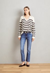 Stripet V-hals genser i kremhvit og svart, teksturert stoff; kombinert med blå rette jeans og svarte flate sko.