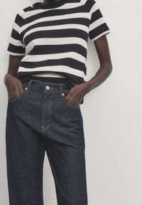 Black and white striped knit top with short sleeves paired with dark blue denim jeans featuring five-pocket styling and a zipper fly.