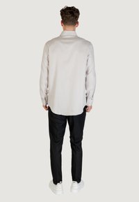 Camicia a righe grigio chiaro con maniche lunghe, pantaloni neri e sneakers bianche. La camicia ha una texture liscia e un orlo curvo.