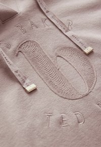 Lichtroze sweatshirt met een gestructureerd groot "10" en een reliëflogo. Inclusief decoratieve trekkoorden met gouden accenten. Zacht materiaal.
