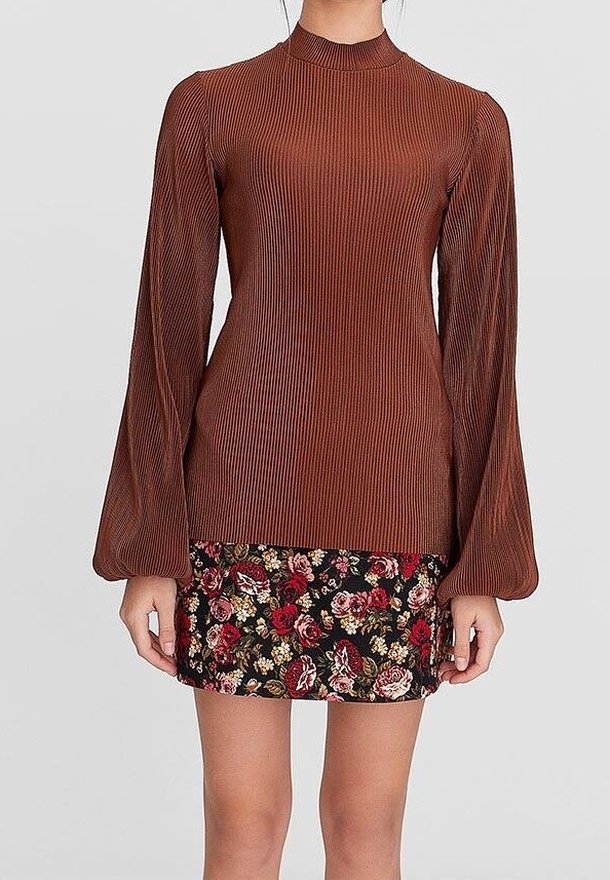 Femme portant un haut côtelé marron à manches longues avec un col montant et une jupe courte noire avec des motifs floraux rouges et blancs.