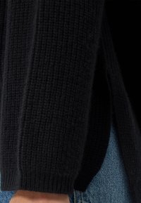 Schwarzer gestrickter Pullover mit strukturiertem Finish, der Rippen entlang des Saums und der Ärmel aufweist, kombiniert mit blauer Denim.