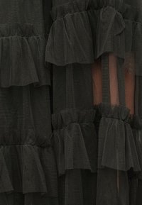 Sort tylstof med lagdelte flæser. Teksturen er blød og gennemsigtig med et ensartet mønster af sammenrynkede kanter over det hele.