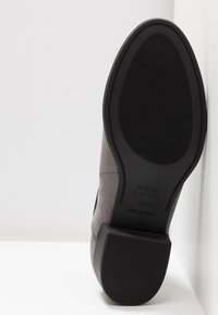 Semelle d'une chaussure en daim gris avec talon et semelle en caoutchouc noir, affichant la marque "New Look", taille 4/37 et inscriptions "Made in China".