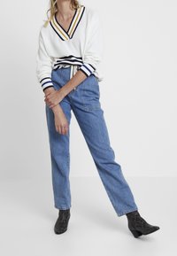 Vit stickad tröja med marinblå och gula ränder vid kragen och ärmsluten, kombinerad med ljusblå högmidjade jeans och svarta ankle boots med ormskinnsprint.