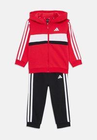 Red Adidas hoodie with white and black stripes, paired with black joggers featuring white stripes and logo. Designed for active wear.