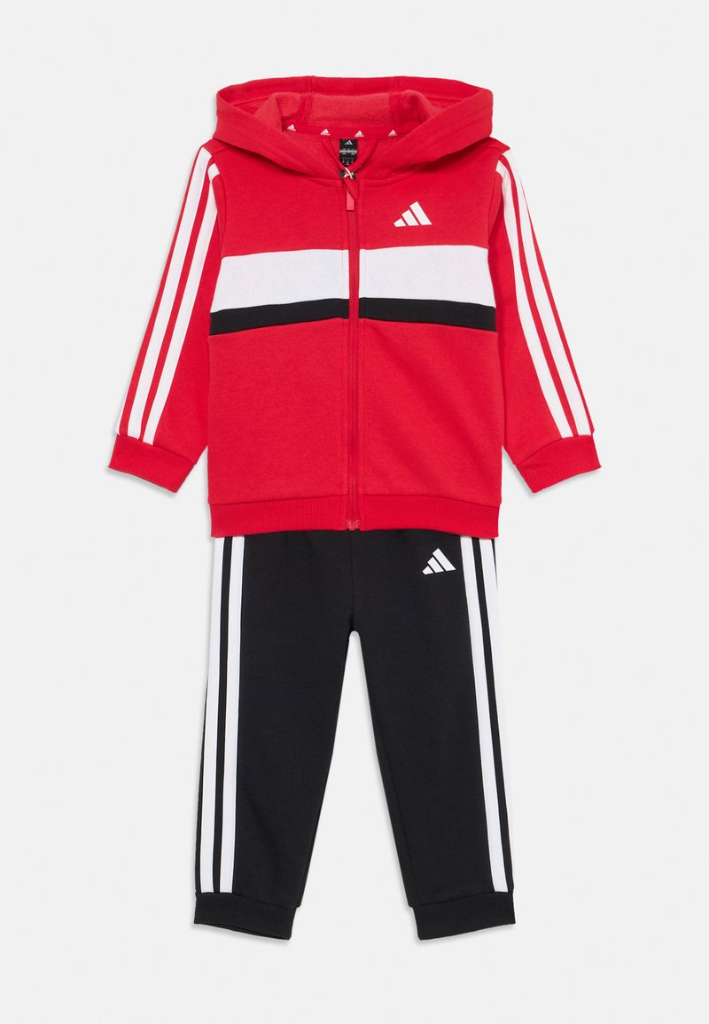 Κόκκινο hoodie Adidas με λευκές και μαύρες ρίγες, συνδυασμένο με μαύρα joggers με λευκές ρίγες και λογότυπο. Σχεδιασμένο για αθλητική χρήση.