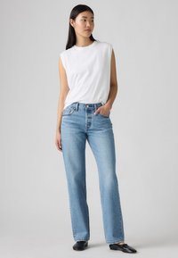 Vaqueros de pierna ancha de color azul claro hechos de denim, con una cintura alta y diseño de cinco bolsillos, combinados con una camiseta sin mangas ajustada blanca.