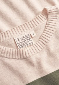 Suéter rosa claro con cuello acanalado y franja horizontal verde. Presenta una etiqueta cosida con instrucciones de cuidado y tamaño 'S'.
