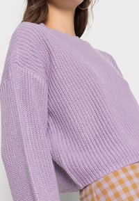 Maglione lavorato a maglia lavanda con vestibilità ampia, caratterizzato da un collo a coste e maniche lunghe, tessuto texturizzato, abbinato a una gonna a quadri.