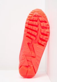 Röd gummisula på sneakers med texturerade greppmönster och en framträdande Nike-logotyp. Konturerad design med fåror för grepp och stöd.