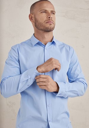 Light blue long-sleeve shirt with a button-down collar, featuring a smooth texture and buttoned cuffs, set against a plain background.