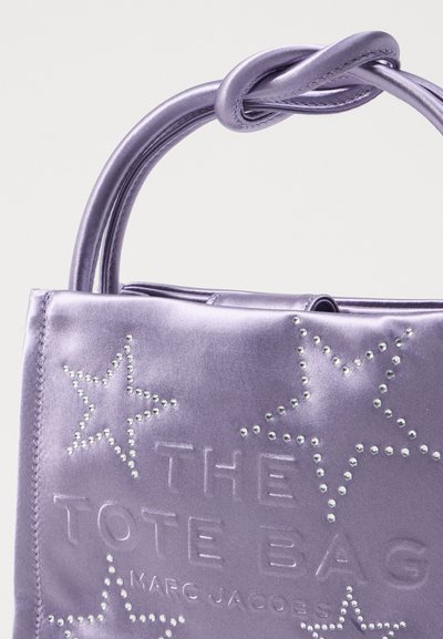 Bolso de tote de satén morado con acentos de estrellas con tachuelas y texto en relieve. Presenta un asa retorcida para un detalle adicional.