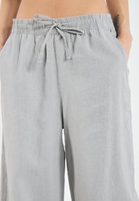 Pantalons en lin gris clair avec une taille élastique et un cordon de serrage, dotés de poches latérales et d'une coupe décontractée. Texture douce et respirante.