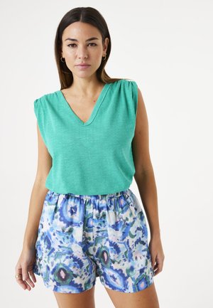 Haut turquoise à col en V avec des détails froncés aux épaules, associé à un short léger avec un motif abstrait bleu et vert.