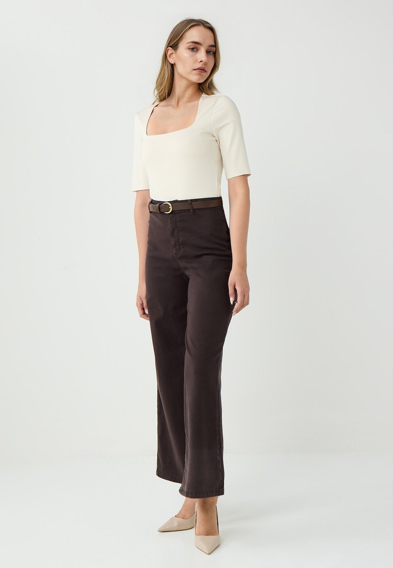 Off-white vierkante hals top met korte mouwen, gecombineerd met hoog-waist, donkerbruine broek en een bruine riem met een gouden ronde gesp.