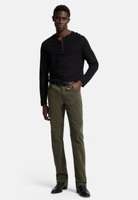 Maglietta henley nera a maniche lunghe con tre bottoni abbinata a pantaloni verdi oliva e stivali in pelle nera. Design semplice e aderente con una trama sottile.