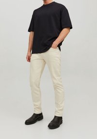 Svart kortärmad t-shirt, krämfärgade slim-fit byxor och svarta ankelboots, med enkelt mönster och släta texturer.