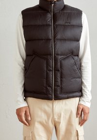 Svart pufferväst med hög krage, dragkedja och två framfickor. Tillverkad av quiltat material, med vertikal sömnad för textur.