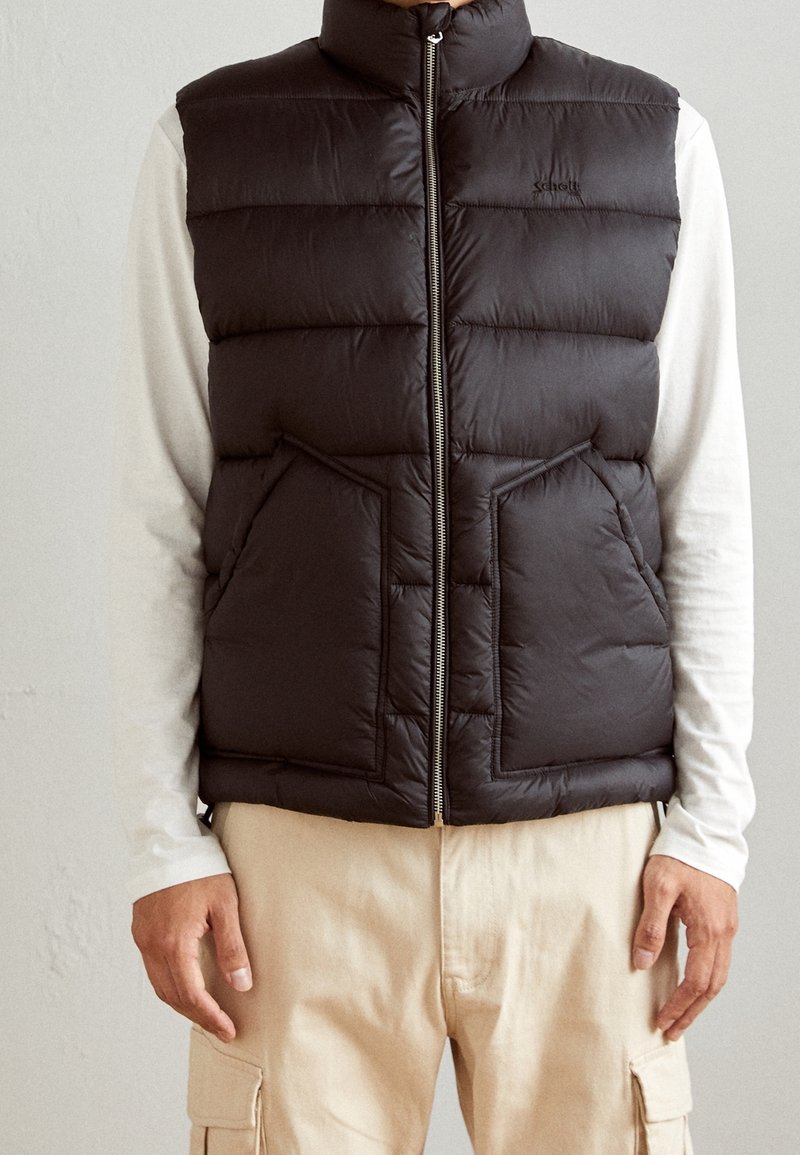 Svart pufferväst med hög krage, dragkedja och två framfickor. Tillverkad av quiltat material, med vertikal sömnad för textur.