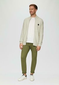 Gestrickter, hellgrauer Reißverschluss-Cardigan, weißes T-Shirt, olivgrüne Hose und weiße Sneakers mit schwarzen Akzenten; lässiges Outfit mit modernem Design.