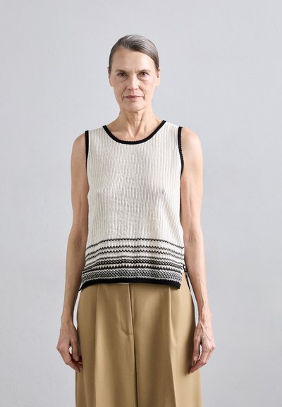 Débardeur en tricot crème avec bord noir et motif rayé horizontal à l'ourlet, associé à un pantalon large beige.