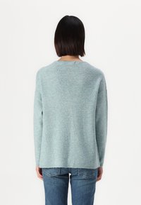 Pull en maille côtelée bleu clair, à encolure ronde et manches longues, avec une coupe décontractée et un ourlet arrière légèrement plus long.