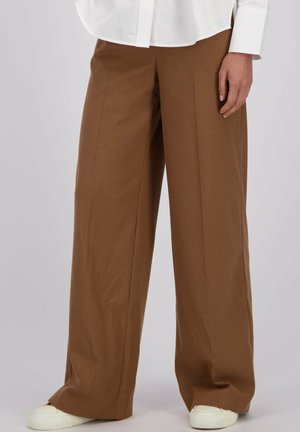 Pantalons larges en tissu brun chaud, avec une texture douce et une coupe ajustée, assortis à des baskets blanches.