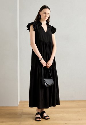 Black maxi dress with ruffled sleeves, V-neck, and gathered waistline. Paired with a black crossbody bag and black sandals on a wooden floor.