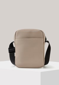 Borsa a tracolla beige con finitura opaca, forma rettangolare, chiusura superiore a zip e tracolla nera regolabile a contrasto con dettagli del logo.