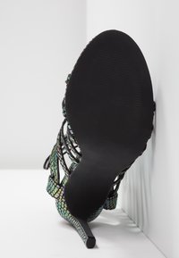 Vue de la semelle d'une sandale à talon haut avec une semelle noire texturée et des brides irisées multicolores à motif peau de serpent.