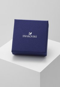 Caixa de joias texturizada em azul-marinho com forma retangular, apresentando um logótipo Swarovski branco e uma superfície padronizada.