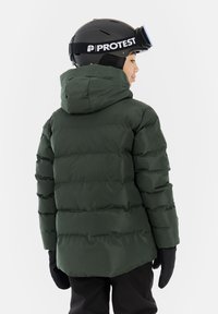 Grønne puffedragt med vandret quiltede sektioner og hætte. Sorte handsker og hjelm med et synligt mærkelogo.