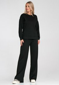 Czarny strój sportowy z luźną bluzą o długich rękawach i spodniami z szerokimi nogawkami, wykonany z miękkiego, teksturowanego materiału.