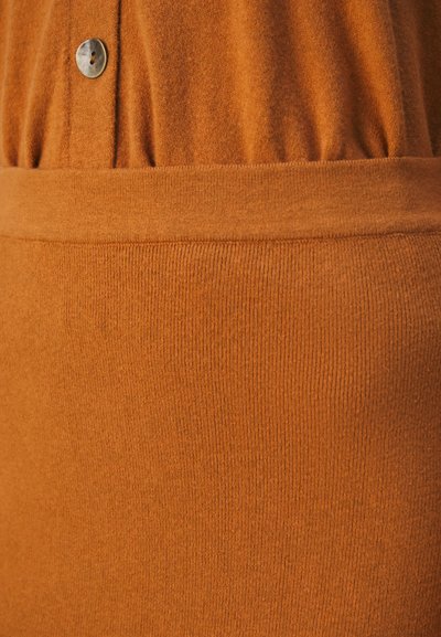 Tissu de couleur rouille avec une surface douce et texturée. Comprend une section froncée avec un bouton en métal en haut et une taille côtelée.
