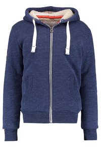 Sudadera con cremallera de color navy, con cordones blancos, forro interior suave, dos bolsillos frontales y puños y dobladillo de canalé. Logo en la manga izquierda.