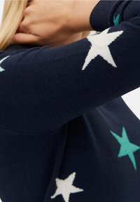 Navy knitted sweater featuring white and teal star patterns on the sleeves. The texture appears soft, with a classic round neckline.