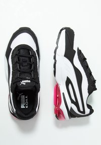 Ett par svart och vitt Puma Cell sneakers med rosa luftkuddarsula, sett från ovan och sidan mot vit bakgrund.