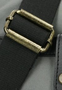 Sangle en tissu noir avec une finition texturée, dotée d'une boucle en métal de couleur dorée et d'un arrière-plan gris, mettant en valeur le détail d'attache de la sangle.