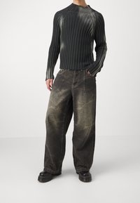 Svart ribbat stickat tröja med långa ärmar, i kombination med mörka, överdimensionerade jeans i denim med en blekt, sliten finish. Klumpiga svarta skor.