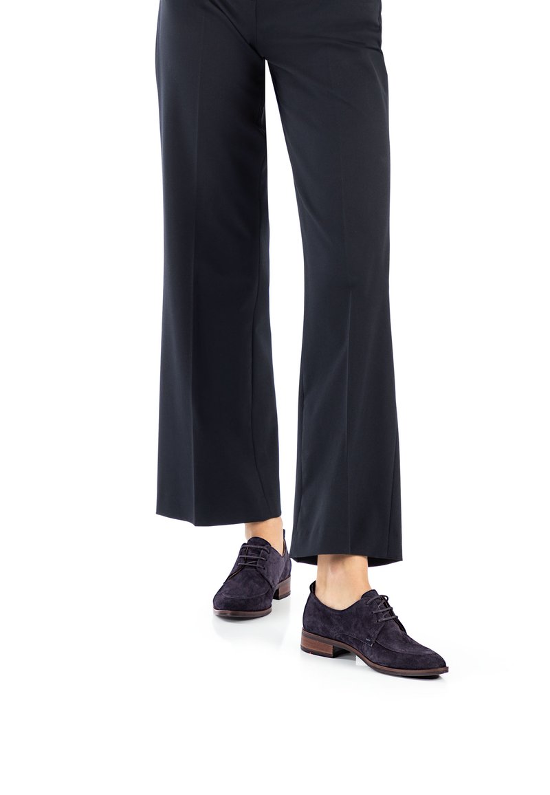 Donkerpaarse suède veterschoenen met een lage, vierkante hak, gecombineerd met zwarte brede pijpen broek. De schoenen hebben een gladde textuur en minimalistische accenten.