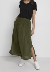 T-shirt noir à col en V associée à une longue jupe vert olive avec des fentes latérales, en tissu fluide. Portée avec des baskets blanches.