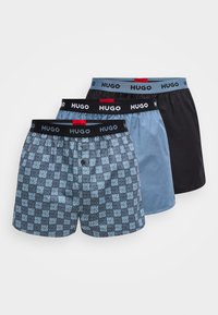 Τρία ζευγάρια ανδρικά boxer: ένα με μπλε και γκρι λογότυπα, ένα μονόχρωμο ανοιχτό μπλε και ένα μονόχρωμο μαύρο. Όλα διαθέτουν μαύρη μέση με την επωνυμία "HUGO".