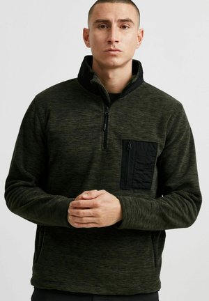 Dark green pullover with a high collar, zippered front, and a black pocket on the chest. Made from textured fabric with a soft finish.