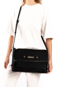 Black leather messenger bag with a flat design, zippered pocket, and metallic hardware accents. Adjustable strap for versatile carrying.