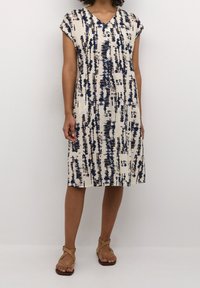 Robe à manches courtes et col en V, de couleur crème avec un motif abstrait bleu et marron. Confectionnée dans un tissu léger, elle tombe juste au-dessus des genoux.