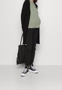 Černý kardigan, zelený žebrovaný top, černé legíny a černé kotníkové tenisky s bílými podrážkami. Nese černou tašku na rameno.