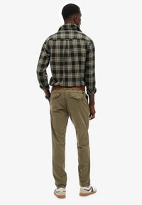 Geruite flanellen overhemd in marineblauw, geel en wit; khaki corduroy broek; gladde textuur; casual pasvorm;bruine riem; witte sneakers met zwarte accenten.