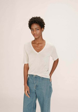 Haut en maille beige à col en V avec des manches courtes, associé à un jeans en denim bleu clair taille haute. Texture douce, coupe décontractée, détails minimalistes.