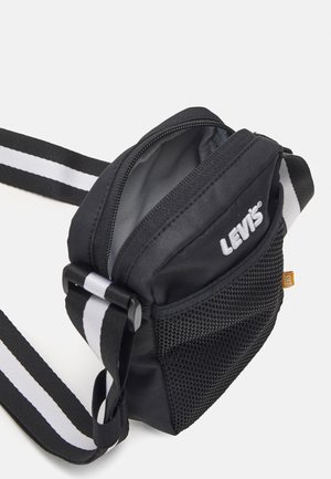 Petit sac bandoulière noir Levi's avec logo blanc, poche avant en mesh et bandoulière réglable rayée noir et blanc.